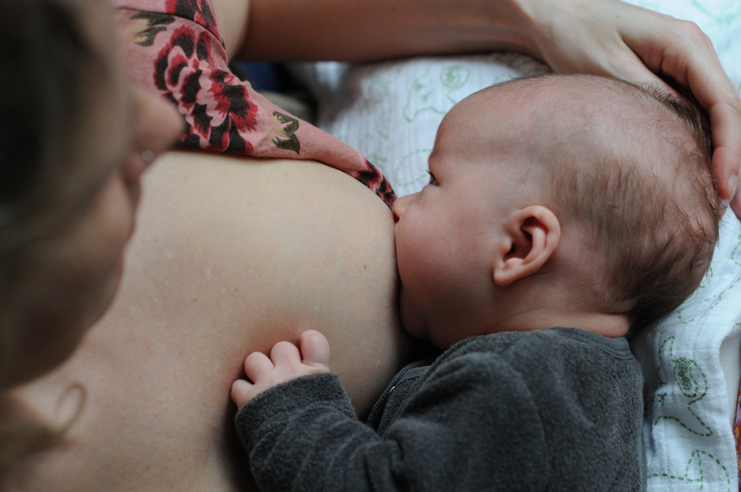 Baby drinkt aan de borst, moeder zit, baby heeft hoofdje op kussen